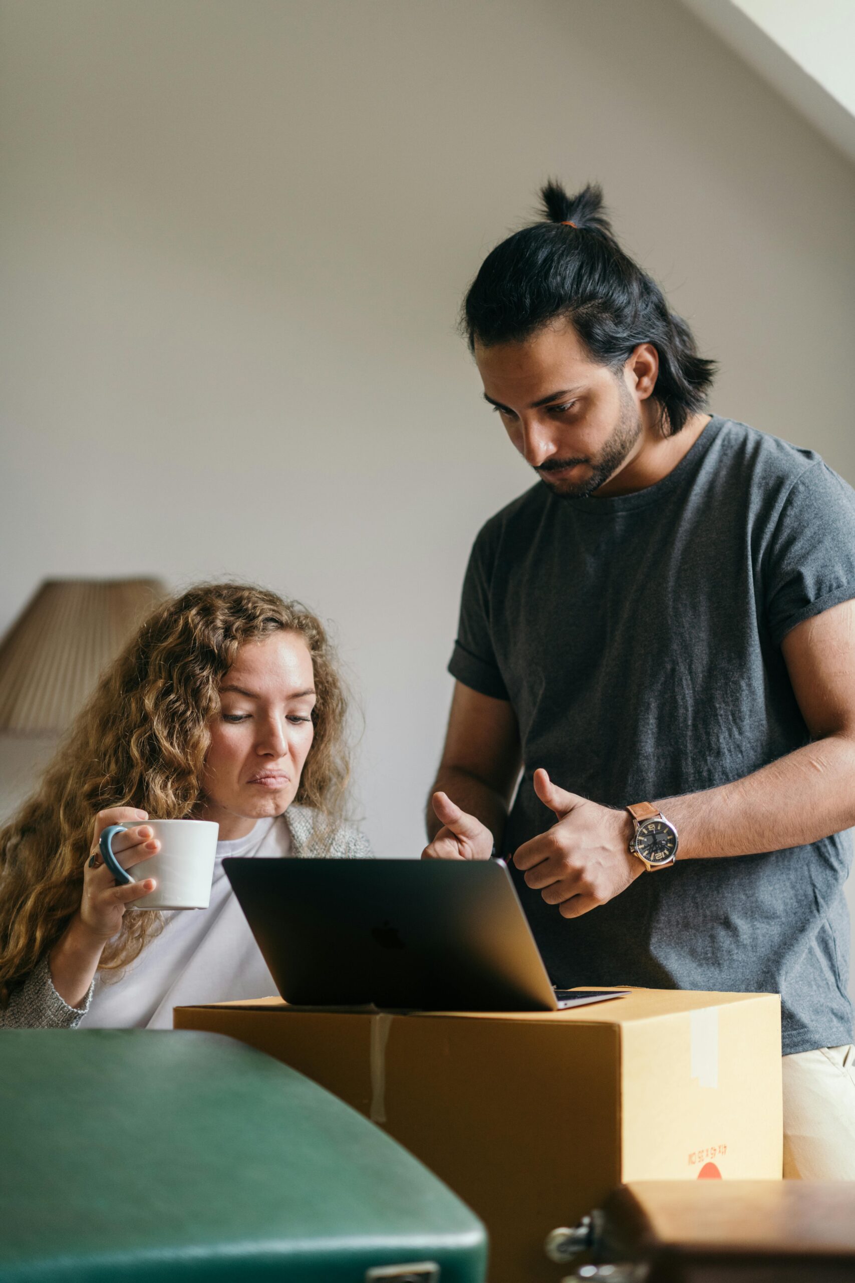 Young couple using a laptop while unpacking in a new home, planning their move online.